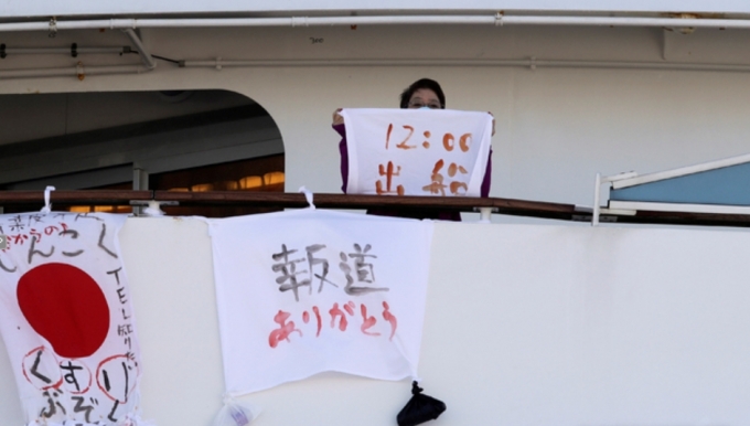 11일 일본 요코하마항에 정박해 있는 유람선 '다이아몬드 프린세스'호에서 한 여성이 출항 시간을 쓴 천을 들고 있다. [AP/뉴시스]