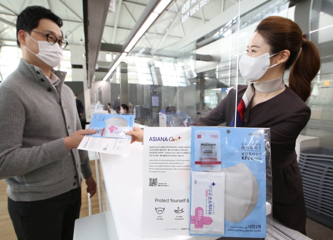 아시아나항공 공항 서비스 직원이 인천국제공항 체크인 카운터에서 마스크·손소독제 등으로 구성된 '케어플러스 키트’를 전달하고 있다. [사진=아시아나항공]