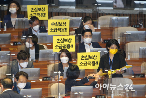 정의당 류호정 의원이 1일 오후 서울 여의도 국회에서 열린  본회의에서 동료의원들에게 '손실보상 소급적용'이라고 기재된 손 피켓을 나눠주고 있다.