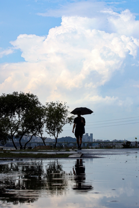 소나기가 내린 지난달 28일 오후 서울 서초구 반포한강공원에서 한 시민이 우산을 쓰고 이동하고 있다. [사진=뉴시스]