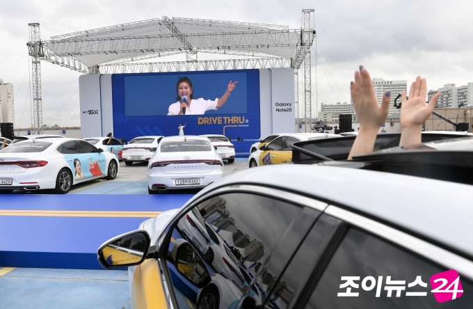 SK텔레콤이 13일 오전 서울 왕십리 비트플렉스 야외주차장에서 드라이브스루 방식으로 갤럭시 노트20을 전달하는 '갤럭시 노트20 드라이브 스루 개통식'을 진행했다. 갤럭시 노트20을 수령한 고개들이 차량에 탄채로 비대면 공연을 즐기고 있다.